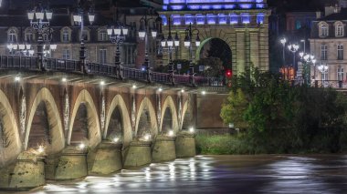 Geceleyin Porte de Bourgogne, Fransa 'nın Bordeaux kentindeki Garonne Nehri' nin üzerindeki süslenmiş sokak lambalarıyla aydınlatılmış Pont de Pierre taş köprüsü. Yansımaların ve şehir ışıklarının çarpıcı zamanlaması