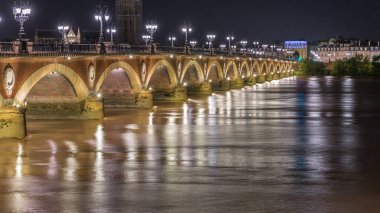 Fransa 'nın Bordeaux kentindeki Porte de Bourgogne' un aydınlatıldığı, gece Garonne Nehri üzerinde süslenmiş sokak lambaları olan Pont de Pierre Stone Köprüsü. Yansımaların ve şehir ışıklarının çarpıcı zamanlaması