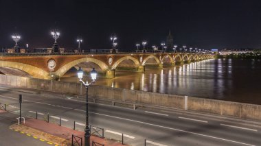 Fransa 'nın Bordeaux kentindeki Porte de Bourgogne' un aydınlatıldığı, gece Garonne Nehri üzerinde süslenmiş sokak lambaları olan Pont de Pierre Stone Köprüsü. Yansımaların ve şehir ışıklarının panoramik zaman çizelgesi