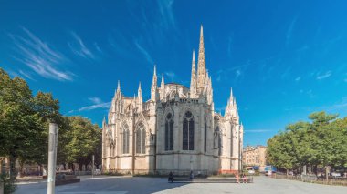 Cathedrale Saint-Andre de Bordeaux timelapse hyperlapse with twin spires under a vibrant blue sky. Green trees and people walking in the square create a serene urban atmosphere. Bordeaux, France clipart