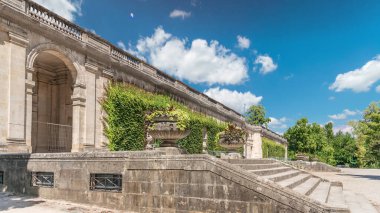Fransa 'nın başkenti Jardin' de Palais du Capitole 'de zaman atlaması. Sarmaşık kaplı yeşil ağaçlar, merdivenler ve parlak mavi bulutlu gökyüzü ile çevrili tarihi bir binanın manzarası.