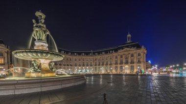 Panorama, Place de la Bourse 'u ve Fransa' nın Bordeaux şehrindeki çeşmeleri gösteriyor. Aydınlatılmış tarihi binalar büyük meydanın sınırında. Trafik ve sokakta hareket sahneyi güçlendirir