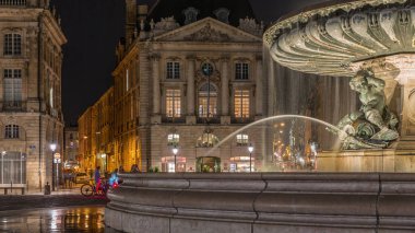 Place de la Bourse manzarası ve Fransa 'nın Bordeaux şehrindeki çeşme zamanı. Aydınlatılmış tarihi binalar büyük meydanın sınırında. Lokantada parlayan pencereler