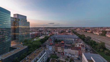 Brüksel kentsel manzarasının yerleşim alanlarıyla ofis gökdelenlerini harmanlayan hava gününden geceye geçiş zamanı. Yeşil park çimenleri, tarihi çatılar ve Belçika 'nın modern mimarisi.