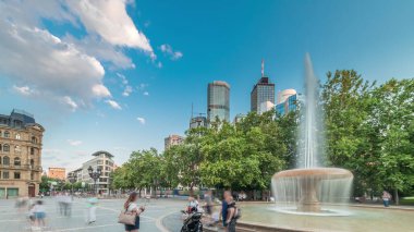 Frankfurt, Almanya merkezindeki Opera Meydanı (Opera Meydanı) zaman atlaması, arka planda gökdelenler ve kulelerle çevrili ve akşam gökyüzü altında ağaçlarla çevrili bir çeşme ve şehir hayatı sergiliyor.