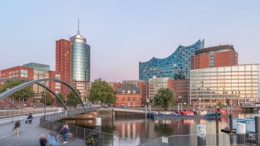 Jan Fedder Promenade day to night transition timelapse hyperlapse in Hamburg, Germany, a vibrant waterfront area. Ships and boats on the Elbe River after sunset with famous buildings in background clipart