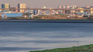 Lizbon 'daki Park Tejo ve River Timelapse' ın arka planında Milletler Bölgesi Modern Mimari Parkı var. Percurso Ribeirinho de Loures 'ten Vasco da Gama Köprüsü