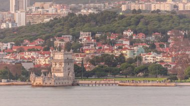 Portekiz 'in Lizbon kentindeki Belem Kulesi' nin havadan görünüşü, Tagus Nehri kıyısındaki ünlü UNESCO simgesi. Sahilde ve yemyeşil parkta gezinen insanların büyüleyici günbatımı sahnesi, tarihi ve güzelliği harmanlıyor.