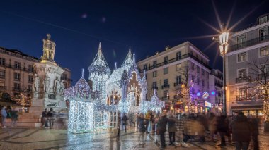Lizbon, Portekiz 'deki Luis de Camoes meydanında aydınlatılmış şatoyla Noel süslemelerinin gece süreleri. İnsanlar şenlikli ışıkların ve tarihi mimarinin etrafında dolanıyor. Ön görünüm