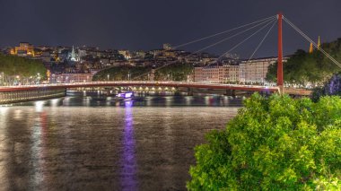 Saone Nehri üzerindeki kırmızı asma köprü ile Lyon 'un şehir manzarasının gece zaman çizelgesi, gece boyunca aydınlatılmış deniz kenarı suya yansıdı. Fransa