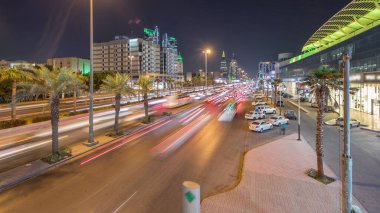 Riyad, Suudi Arabistan 'ın şehirsel gece zaman çizelgesinde aydınlık kuleler, gökdelenler, Kral Fahd Yolu ve yoğun trafik yer alıyor. Palmiyeler ve sokak lambaları alışveriş merkezinin yakınındaki ana otoyolda.
