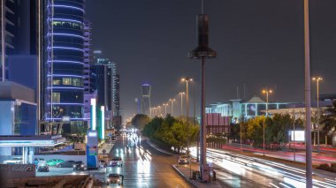 Suudi Arabistan 'ın Riyad kentindeki ikonik bükümlü gökdeleniyle King Fahd Yolu' ndaki yoğun karayolu trafiğinin hava takvimi görüntüsü. Dünyanın en yüksek sekizinci büküm kulesi. Aydınlatılmış sokaklar ve ağaçlar