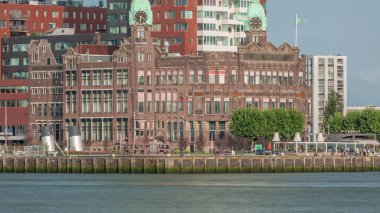 Rotterdam 'daki Otel New York' un tarihi cephesinin zamanı. Eski Hollanda-Amerika Hat Karargahı. Tekneler geçerken insanlar rıhtımda dinleniyor. Limanın yanındaki ikonik mimari