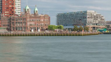 Rotterdam şehir merkezindeki Otel New York 'un tarihi cephesine sahip modern binaların zaman çizelgesi. Eski Hollanda-Amerika Hat Karargahı. Tekneler geçerken insanlar rıhtımda dinleniyor. Simgesel mimari