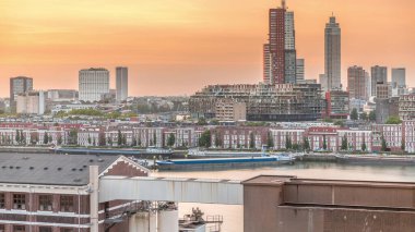 Günbatımında Rotterdam şehir merkezindeki modern binaların hava zaman çizelgesi, Hollanda. Finans bölgesinde kuleler ve gökdelenler, turuncu gökyüzü ile eski fabrika canlı bir ufuk çizgisi oluşturur