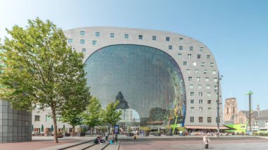 Rotterdamse Markthal 'ın dış yüzeyinde aşırı kayma. Dükkanları ve restoranları olan ikonik at nalı şeklinde bir bina. Meydanda gezinen insanlar. Gökdelenler ve arka planda canlı bir şehir manzarası