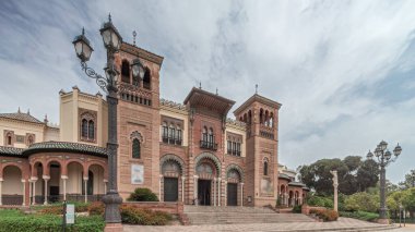 Maria Luisa Park 'taki Sevilla Sanat ve Gelenekler Müzesi cephesi. Plaza de America 'da Mudejar tarzı bir bina var. Bulutlu gökyüzü altında zaman atlaması. Sevilla, İspanya.