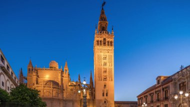 La Giralda ve Seville Katedrali günden geceye geçiş zamanı, gün batımından sonra altın ışıklarla parıldıyor. Tarihi çan kulesi, gotik detaylar ve Seville, İspanya 'da aydınlatılmış sokaklar.