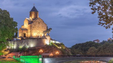 Metekhi Virgin Mary Assumption Church day to night transition timelapse and the Statue of King Vakhtang Gorgasali above the Kura River after sunset. Traffic on a bridge. Tbilisi, Georgia. clipart