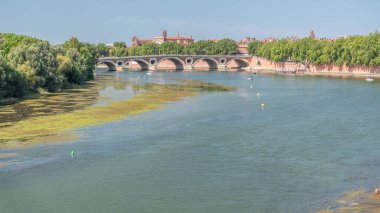 Toulouse, Fransa 'da Garonne River ve Pont Neuf saatleri. Rönesans kemer köprüsü mavi gökyüzünün altındaki suya Daurade Leydisi Bazilikası ile yansıyor. Yeşil ağaçlı rıhtım