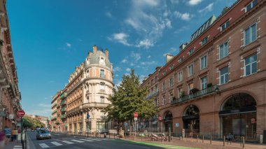 Toulouse, Occitanie, Fransa 'da Rue de Metz' in zaman çizelgesini gösteren panorama, tarihi cepheleri, dükkanları, kafeleri, trafiği ve mavi bulutlu gökyüzünü gösteriyor. Şehrin göbeğinde canlı bir şehir manzarası