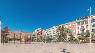 Panorama, İspanya, Valencia 'daki Plaza de la Reina' nın zaman çizelgesini gösteriyor. Tarihi bir kilise kulesi, hareketli kafeler ve sıcak Akdeniz mavi gökyüzünün altında merkezi bir çeşmesi olan canlı bir meydan..