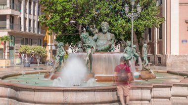Valencia, İspanya 'daki ikonik Turia Pınarı ile birlikte Plaza de la Virgen' den Timelapse. Neptün heykeli Turia Nehri ve kanallarını temsil eder. İnsanlar yeşil ağaçlarla meydanda geziniyor.