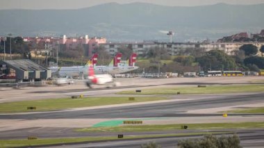 Lizbon Havaalanı Humberto Delgado saatine park etmiş uçaklar hareket ediyor. Pist aktivitesi, terminaller, şehrin ufuk çizgisi inşaatı ve temiz bir gökyüzü altında hareket halindeki farklı havayollarının uçakları. Portekiz