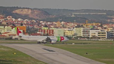 Lizbon Humberto Delgado Havaalanı 'nda arka planda tepeler ve şehir manzarası olan bir uçak hareket ediyor. Portekiz 'de güneşli bir günde havalanmadan önce uçak taksisi. Yandan görüntüle