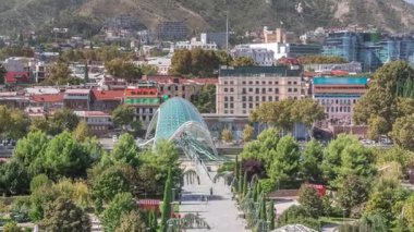 Barış Köprüsü 'nün zamanı, Kura Nehri üzerinde yay şeklinde bir çelik ve camdan köprü, Tiflis, Georgia' daki Rike Park 'tan Eski Şehir' e yürüyen insanlar.