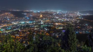 Tiflis şehir manzarası, Gürcistan günden geceye zaman. Şehir merkezinin ve Tiflis 'teki Kura Nehri' nin üst manzarası. Gökyüzünden Gürcistan başkentinin gökyüzü manzarası aydınlatılmış ünlü simgelerle
