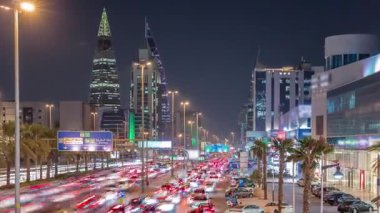 Riyad, Suudi Arabistan 'ın şehirsel gece zaman çizelgesinde aydınlık kuleler, gökdelenler, Kral Fahd Yolu ve yoğun trafik yer alıyor. Palmiyeler ve sokak lambaları şehrin içinden geçen ana otoyol boyunca uzanır..