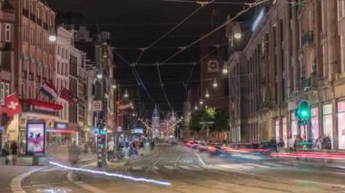 Damrak Caddesi 'ndeki elektrik tramvayı gece vakti Dam Meydanı' ndan Centraal İstasyonu 'na gidiyor. İnsanlar tramvay durağında beklerken trafik yolda ilerliyor. Amsterdam, Hollanda