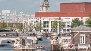 Amstel Nehri 'ndeki Amstel kilitlerinden geçen teknelerin zamanına göre görüntüsü. Opera binası ve Zuiderkerk kulesi arka planda görünüyor. Bulutlar gökyüzünü dolduruyor. Amsterdam, Hollanda