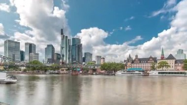 Almanya 'nın Frankfurt kentindeki ana nehir üzerindeki tarihi Eiserner Steg Demir Köprüsü' nün hızlandırılması. Gökdelenler ufuk çizgisi ve tarihi binalar bulutlarla dolu bir zaman dilimi altında suya yansıyor.