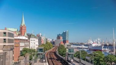 Almanya 'nın Hamburg kentindeki Landungsbrucken istasyonuna gelen trenler son sürat ilerliyor. Metroya binen insanlar mavi gökyüzünün altında Elbphilharmonie, liman ve marina ile panoramik manzara