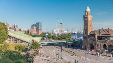 Hamburg, Almanya 'daki St. Pauli Piers Landungsbrucken' in uçuş zamanı. İkonik saat kulesi, yoğun sokak trafiği, limana yanaşmış gemiler ve mavi gökyüzünün altında panoramik manzaralar.