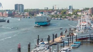 Almanya 'nın Hamburg kentinde Elbe nehir kenarının hava zaman çizelgesi. İskeleye yakın tekneler, Jan Fedder gezinti güvertesi, marina ve konteyner gemilerinin geçtiği manzara. Elbe Nehri kıyısındaki canlı şehir manzarası
