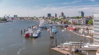 Almanya 'nın Hamburg kentinde Elbe nehir kenarının hava zaman çizelgesi. Rıhtımın yakınındaki Jan Fedder Gezinti Güvertesi, marina ve geçen gemilerle sahile manzara. Elbe Nehri kıyısındaki canlı şehir manzarası