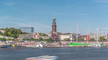 Elbe nehir kenarı ve Hamburg, Almanya 'daki St. Michaels kilise kulesinin panoramik zaman çizelgesi. İskeleye yakın teknelerle manzara, Jan Fedder gezinti güvertesi ve oradan geçen feribotlar. Nehir kenarındaki canlı şehir manzarası