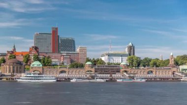 St.Pauli Piers Landungsbrucken 'de Hamburg, Almanya' da feribotlu Skyline zaman çizelgesi. İkonik saat kulesi, yat limanına yanaşan gemiler ve bulutlu mavi gökyüzünün altındaki limanın panoramik manzarası.