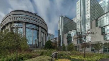 Brüksel 'deki Avrupa Mahallesi' ndeki binalar Avrupa Parlamentosu, Komisyon ve dramatik bulutlu gökyüzü altındaki kurumlarla aynı tarihe denk geliyor. Güneş camdan yansıyor. Leopold Park ön planda çimenlerle