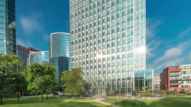 Panorama modern ofis binalarının zaman çizelgesini gösteriyor. Parktaki yeşil ağaçlar tarafından çerçevelenmiş parlak mavi gökyüzü üzerinde yansımaları ve röfleleri olan cam gökdelenler. Brüksel 'de güneş ışığı ve geçen bulutlar