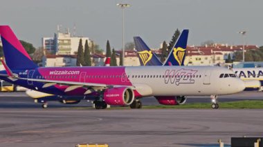 Lizbon, Portekiz - 25 Şubat 2025: Yoğun bir Lizbon havalimanında yolcu uçakları Wizzair taksileri, terminaller, diğer uçaklar ve arka planda bir şehir manzarası. Havanın canlı atmosferi