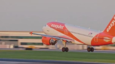 Lizbon, Portekiz - 25 Şubat 2025: Bir ticari uçak EasyJet gün batımında Lizbon Havaalanı 'na iniş yaptı ve lastik dumanı yere indi. Terminaller ve açık bir gökyüzü burada canlı bir zemin oluşturur.