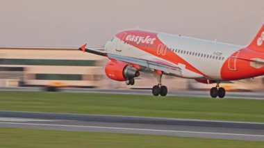 Lizbon, Portekiz - 25 Şubat 2025: Bir ticari uçak EasyJet gün batımında Lizbon Havaalanı 'na iniş yaptı ve lastik dumanı yere indi. Terminaller ve açık bir gökyüzü burada canlı bir zemin oluşturur.