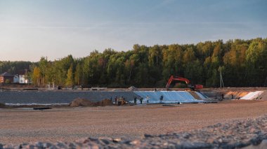 Panoramik manzara kazıcılar ve buldozerlerle şehir alanına dönüşür. Büyük bir tarladaki yeni kır köyü için şantiye manzarası. Yeşil orman ve mavi gökyüzü
