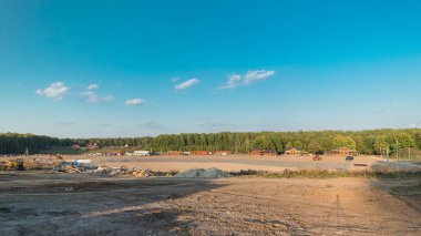 Panoramik peyzaj, mekanik zaman ayarlı kentsel alana dönüşür. Büyük bir tarlada ahşap evleri olan yeni kır köyü için şantiye manzarası. Mavi gökyüzünde güzel bulutlar