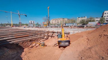 Sarı ve turuncu kazıcılar büyük hendek tünelinde çalışıyor. Yeraltı metro istasyonunun inşaat alanındaki kalın kiriş ve yapılardan oluşan demir borulardan yapılar takviye ediliyor.