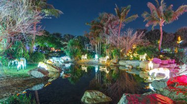 Zebralar ve ağaçlarla dolu bir göl. Dubai Işıltılı Bahçesi 'nde aydınlanmış ağaçlar ve heykeller. Çevreye duyarlı mimarinin yer aldığı sanat eseri, geri dönüşümlü ürünlerden yapılar yaratıyor